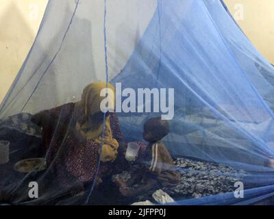 Baidoa, Somalia. 29.. Juni 2022. Eine somalische Mutter sitzt mit ihrem Baby unter einem Moskitonetz auf einem Klinikbett im Sahal-Macalin-Stabilisierungszentrum in Baidoa im Südwesten Somalias. Die Klinik behandelt stark unterernährte Kinder. Das Land am Horn von Afrika erlebt seit Monaten eine schwere Dürre. Vier Regenzeiten in Folge sind nicht eingetreten. Jetzt sind vor allem kleine Kinder vom Hungertod bedroht. (To dpa 'Wettlauf gegen die Zeit um das Leben hungernder Kinder') Quelle: Eva-Maria Krafczyk/dpa/Alamy Live News Stockfoto