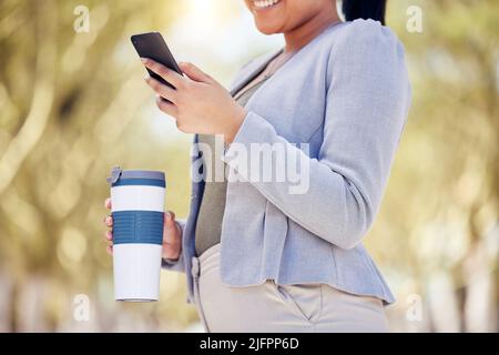 Überprüfen ihres digitalen Zeitplans. Nahaufnahme einer unkenntlichen Geschäftsfrau, die ein Mobiltelefon benutzt, während sie im Freien aus einem wiederverwendbaren Becher trinkt. Stockfoto