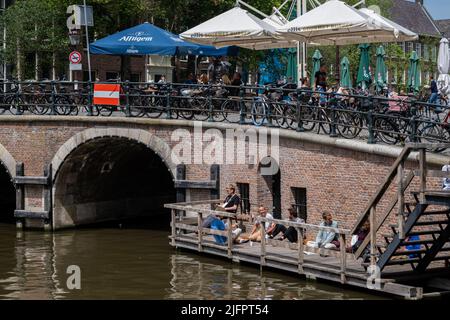 Amsterdam, Niederlande - 21. Juni 2022: Alte Brücke im Zentrum von Amsterdam mit Leuten, die am Wasser sitzen Stockfoto