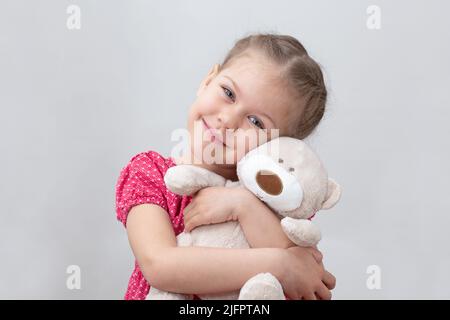 Glückliches Kind umarmt Teddybär auf weißem Hintergrund kaukasischen kleinen Mädchen von 5-6 Jahren in rot Blick auf die Kamera Stockfoto