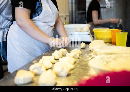 Der Prozess der Brotherstellung. Den Weizenteig für Brötchen in Stücke teilen. Vorderansicht. Stockfoto