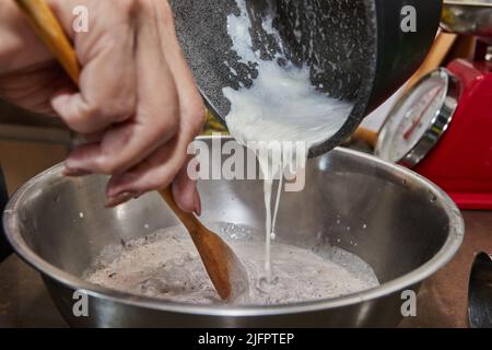 Der Koch gießt Schlagsahne in eine Schokoladenkuchenmischung mit Birnen und Nüssen. Schritt für Schritt Rezept Stockfoto