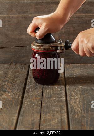 Die Hände der Frauen Rollen den Deckel auf einem Glas Himbeermarmelade. Konservierung, Kochen, Essen Stockfoto