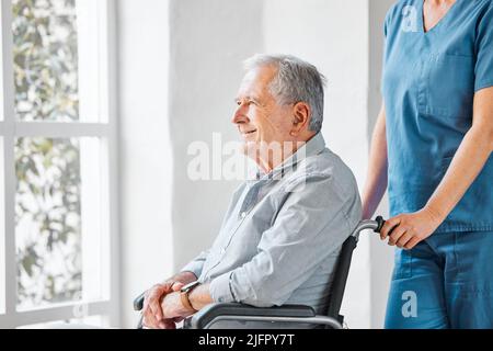 Der Tag fühlt sich besser an, nachdem ich die Welt bewundere. Aufnahme einer Krankenschwester, die in einem Altersheim in einem Rollstuhl für einen älteren Mann sorgt. Stockfoto