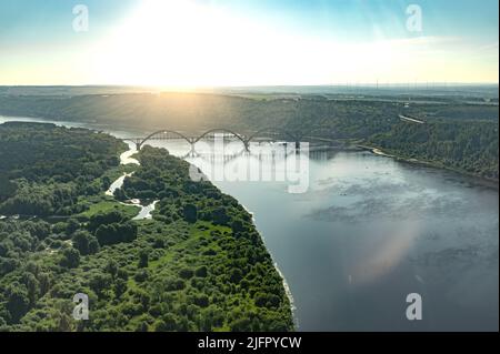 Luftaufnahmen aus einem Flugzeugfenster. Flugflug über den Fluss mit Brücke bei Sonnenuntergang im Sommer Stockfoto