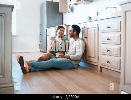 Lacht mit mir, Bleib bei mir. Aufnahme eines jungen Paares, das zu Hause eine Tasse Kaffee zusammen trinkt. Stockfoto