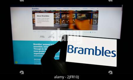 Person, die Mobiltelefon mit dem Logo des australischen Dienstleistungsunternehmens Brambles Limited auf dem Bildschirm vor der Business-Webseite hält. Konzentrieren Sie sich auf die Telefonanzeige. Stockfoto