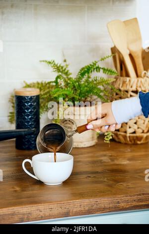 Nahaufnahme der Hand, die Kaffee in eine Tasse gießt. Morgendliches Routinekonzept. Stockfoto