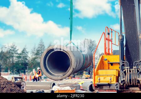 Betonabflussrohr, das während der Tiefentwässerung auf der Baustelle vom Bagger angehoben wurde Stockfoto