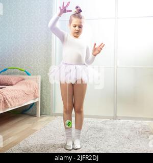 Eine kleine Ballerina im weißen Badeanzug tanzt zu Hause, lernt tanzen und spielt Jo-Jo. Tanzunterricht zu Hause. Stockfoto