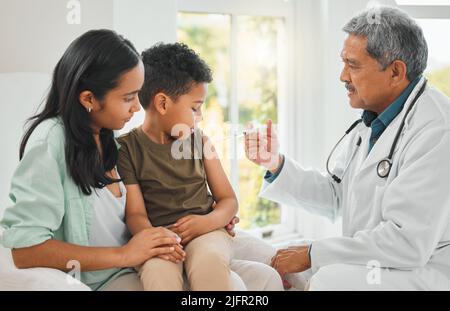 Das wird nicht lange dauern. Aufnahme eines reifen männlichen Arztes, der einem kleinen Jungen eine Injektion in einem Krankenhaus verabgab. Stockfoto