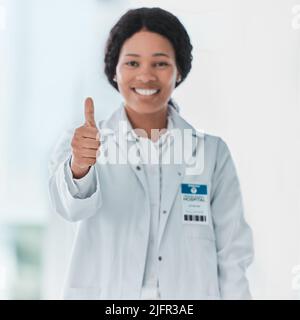 Einige Helden tragen weiße Mäntel. Porträt eines jungen Arztes, der in einem Krankenhaus Daumen nach oben zeigt. Stockfoto