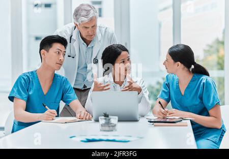 Kooperierendes und produktives Arbeiten zur Verbesserung des Patienten. Aufnahme einer Gruppe von Ärzten, die in einem zusammen an einem Laptop arbeiten Stockfoto