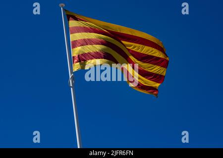 Die Flagge Kataloniens (Autonome Gemeinschaft Spaniens) winkt in einem tiefblauen Himmel. Fahnenstange nach links geneigt. Stockfoto