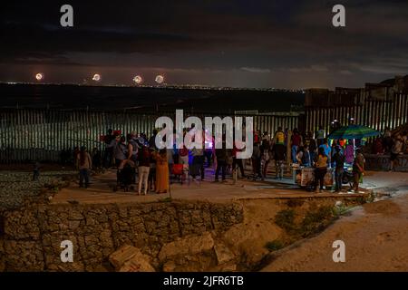 Tijuana, Mexiko. 04.. Juli 2022. Hunderte von Menschen beobachten vom Grenzzaun in Playas de Tijuana, Mexiko, wie in der Bucht von San Diego, Kalifornien, ein Feuerwerk zum US-Unabhängigkeitstag gestartet wurde. An der Veranstaltung nahmen zahlreiche Deportierte aus den Vereinigten Staaten Teil. Außerdem kamen ein Dutzend Migranten verschiedener Nationalitäten an die Wand, um weniger Todesfälle und Einwanderungsreformen in den Vereinigten Staaten zu fordern. Quelle: Omar Martinez/dpa/Alamy Live News Stockfoto