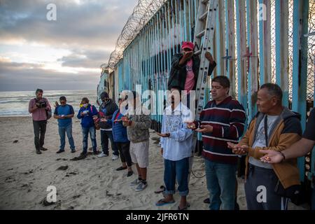 Tijuana, Mexiko. 04.. Juli 2022. Ein Dutzend Migranten verschiedener Nationalitäten stehen am Strand von Tijuana an der Grenzmauer zu den USA, um der Todesfälle zu gedenken und eine Einwanderungsreform in den USA zu fordern.die USA feiern am 4. Juli ihren Unabhängigkeitstag. Quelle: Omar Martinez/dpa/Alamy Live News Stockfoto