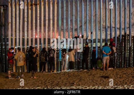 Tijuana, Mexiko. 04.. Juli 2022. Hunderte von Menschen beobachten vom Grenzzaun in Playas de Tijuana, Mexiko, wie in der Bucht von San Diego, Kalifornien, ein Feuerwerk zum US-Unabhängigkeitstag gestartet wurde. An der Veranstaltung nahmen zahlreiche Deportierte aus den Vereinigten Staaten Teil. Außerdem kamen ein Dutzend Migranten verschiedener Nationalitäten an die Wand, um weniger Todesfälle und Einwanderungsreformen in den Vereinigten Staaten zu fordern. Quelle: Omar Martinez/dpa/Alamy Live News Stockfoto