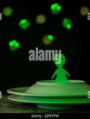Ein lustiges grünes Alien aus Pappe ist auf einem Raumschiff mit zwei überlappenden Platten Stockfoto