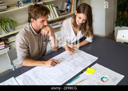 Eine Gruppe von Geschäftsleuten, die sich mit dem Architekten des Bauingenieurs treffen und nach Plänen suchen Stockfoto