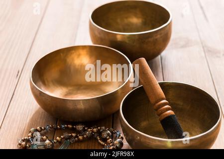 Stillleben mit drei tibetischen Bronzeschalen auf einem Holztisch. Die Klangschalen werden in Meditations- und Musiktherapiesitzungen eingesetzt. Stockfoto