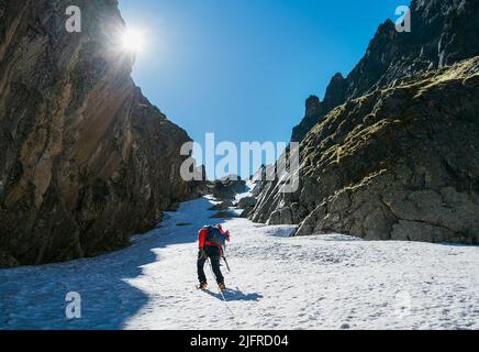 Team Roping up Frau mit Kletteraxt gekleidet Höhenbergsteigen Kleidung mit Rucksack zu Fuß durch verschneiten Hang im Couloir mit Hintergrundbeleuchtung Stockfoto