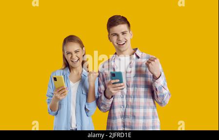Junge Freunde kaukasischen Mann und Frau überglücklich hält Handy, stehen in gelben Studio Stockfoto