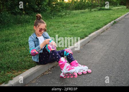 Hübsches kleines Mädchen, das an einem schönen Sommertag in einem Park Rollschuh lernt. Stockfoto