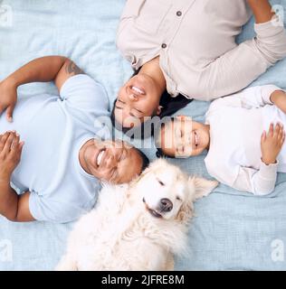 Wo verstecken sie meine Leckereien. Aufnahme einer jungen Familie, die mit ihrem Hund zu Hause im Garten auf dem Gras liegt. Stockfoto