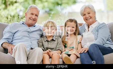 Porträt einer liebevollen vierköpfigen Familie, die bequem auf ihrem Sofa im Wohnzimmer zu Hause sitzt. Eine Großmutter, Großvater, Enkel und Stockfoto
