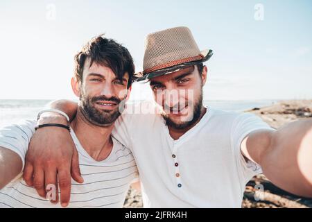 Ein paar junge Freunde, die sich beim Sonnenuntergang am Strand umarmen und ein Selfie machen. Freundschaft und Liebeskonzept Stockfoto