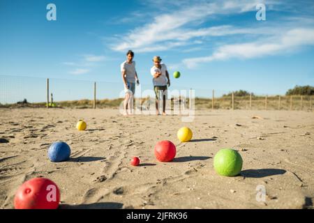 Touristen spielen ein aktives Spiel, Petanque auf einem Sandstrand am Meer - Gruppe von jungen Menschen spielen Boule im Freien in Strandurlaub Stockfoto