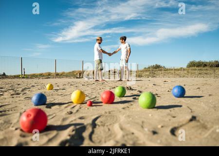 Touristen spielen ein aktives Spiel, Petanque auf einem Sandstrand am Meer - Gruppe von jungen Menschen spielen Boule im Freien in Strandurlaub Stockfoto