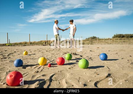 Touristen spielen ein aktives Spiel, Petanque auf einem Sandstrand am Meer - Gruppe von jungen Menschen spielen Boule im Freien in Strandurlaub Stockfoto