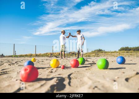 Touristen spielen ein aktives Spiel, Petanque auf einem Sandstrand am Meer - Gruppe von jungen Menschen spielen Boule im Freien in Strandurlaub Stockfoto