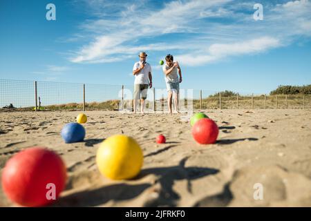 Touristen spielen ein aktives Spiel, Petanque auf einem Sandstrand am Meer - Gruppe von jungen Menschen spielen Boule im Freien in Strandurlaub Stockfoto