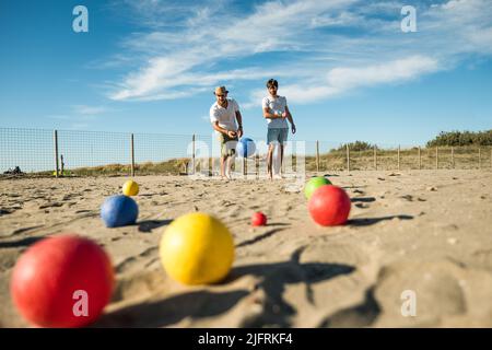 Touristen spielen ein aktives Spiel, Petanque auf einem Sandstrand am Meer - Gruppe von jungen Menschen spielen Boule im Freien in Strandurlaub Stockfoto