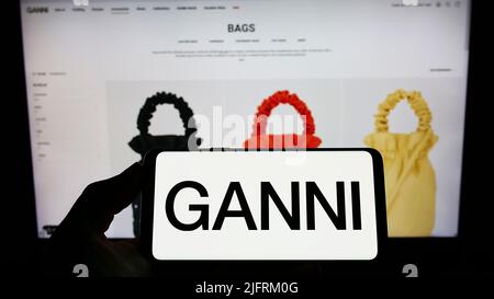 Person, die das Smartphone mit dem Logo des dänischen Modeunternehmens Ganni AUF dem Bildschirm vor der Website hält. Konzentrieren Sie sich auf die Telefonanzeige. Stockfoto