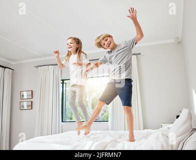 Ich denke, meine Brüder sind verrückt geworden. Aufnahme eines Bruders und einer Schwester, die Spaß haben, während sie zu Hause gemeinsam auf ein Bett springen. Stockfoto