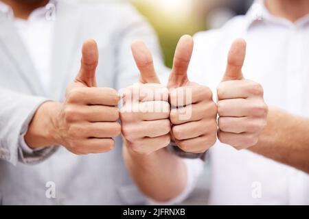 Legen Sie einen Daumen hoch, wenn Sie es mögen. Aufnahme von zwei nicht erkennbaren Geschäftsleuten, die einen Daumen nach oben zeigen. Stockfoto