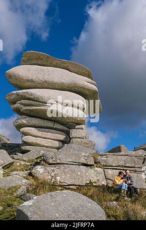 Ein junges Paar, das sich unter dem hoch aufragenden Granitfelsen am Cheesewring entspannt, der von Gletscheraktionen auf Stowes Hill auf Bodmin Moor in Cornwall hinterlassen wurde. Stockfoto