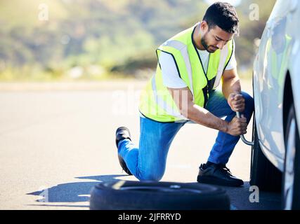 Einige schöne Wege können nicht entdeckt werden, ohne los zu werden. Aufnahme eines jungen Mannes, der in einem ländlichen Gebiet einen Platten Reifen an seinem Auto gewechselt hat. Stockfoto