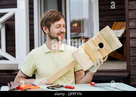 Porträt eines lächelnden Zimmermanns, der ein Vogelhaus aus Holz gebaut hat. DIY-Konzept. Stockfoto