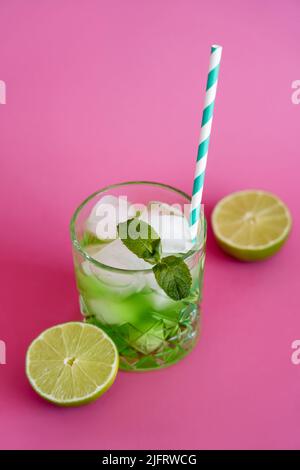 Hochwinkelansicht von gefrorenen Eiswürfeln im Glas mit Minze und grünem Mojito-Getränk auf Pink Stockfoto