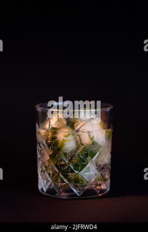 Kühles facettiertes Glas mit Rum und Eiswürfeln isoliert auf schwarz Stockfoto