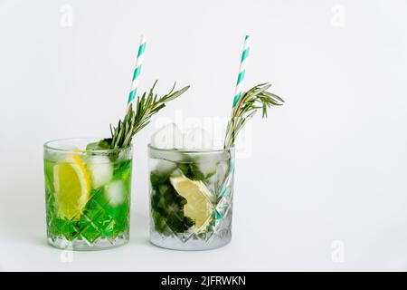 Facettierte Gläser mit Cocktails, Eiswürfeln und Zitrusfrüchten auf Weiß