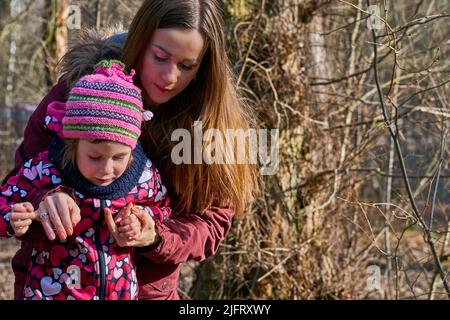 Junge, fürsorgliche Mutter hilft einem Kind im herbstlichen warmen Wald Stockfoto