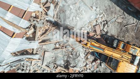 Demolition Building Luftaufnahme von oben. Gelber Bagger zerstören altes Haus. Stockfoto
