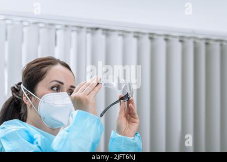 Die Krankenschwester überprüft ihre Schutzbrille, während sie im Aufnahmebüro eine N95-Maske auf ihrem Gesicht trägt. Konzentrieren Sie sich auf Brillen Stockfoto