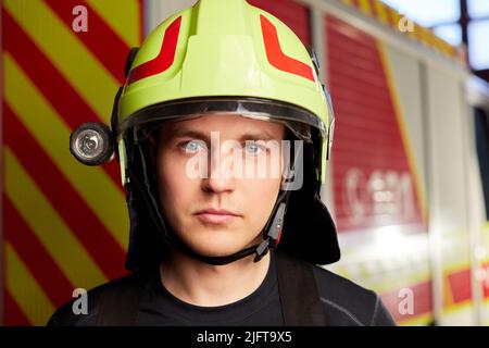 Junger Feuerwehrmann in Uniform, der vor einem Feuerwehrauto steht Stockfoto