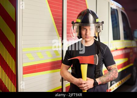 Foto von Feuerwehrmann mit Helm und Axt gegen Feuerwehrmann. Stockfoto